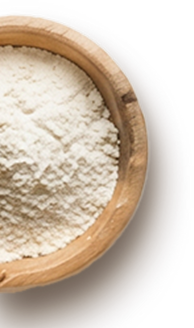 A close-up view of a wooden bowl filled with fine, white flour. The smooth texture of the flour is visible against the natural wood grain of the bowl, creating a simple yet inviting presentation.