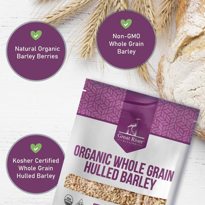 Great River Milling Organic Hulled Barley package on a light wooden surface, surrounded by wheat stalks and a rustic loaf of bread, with purple accents and product details