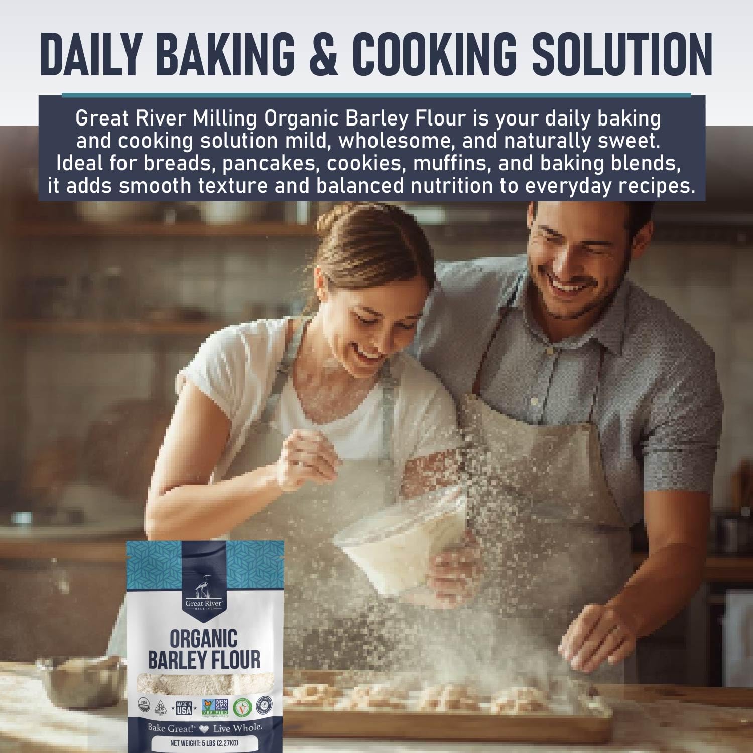 A smiling couple bakes together in a warm kitchen, with a bag of Great River Milling Organic Barley Flour in the foreground. The packaging is blue with white text