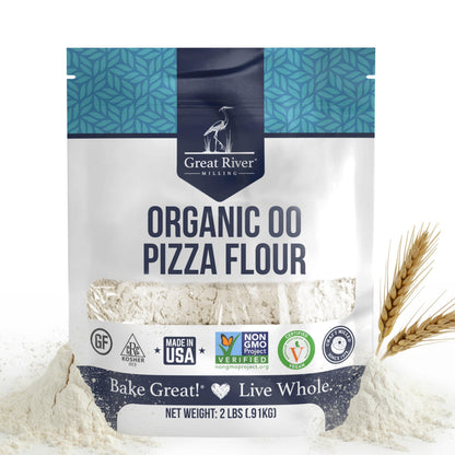 A 2-lb bag of Organic 00 Pizza Flour, crafted from high-quality organic wheat, rests in a mound of flour with two wheat stalks nearby. The package features certifications for organic, kosher, gluten-free, and non-GMO—ideal for creating an authentic Neapolitan pizza crust at home.