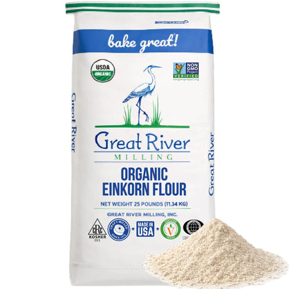 A 25-pound bag of Organic Einkorn Flour stands upright, showcasing organic and non-GMO labels. Ideal for anyone seeking bulk einkorn flour, this ancient wheat flour features a small mound of flour positioned in the bottom right corner in front of the bag.
