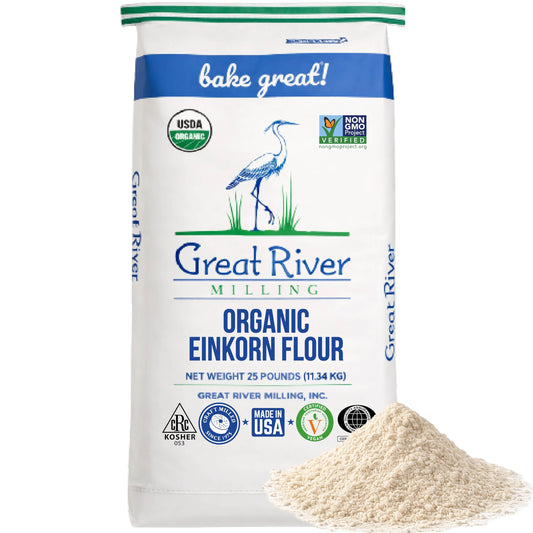 A 25-pound bag of Organic Einkorn Flour stands upright, showcasing organic and non-GMO labels. Ideal for anyone seeking bulk einkorn flour, this ancient wheat flour features a small mound of flour positioned in the bottom right corner in front of the bag.
