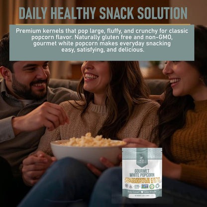 A smiling couple sits on a couch sharing a large bowl of popcorn. In the foreground, a bag of Great River Milling Gourmet White Popcorn Kernels is prominently displayed