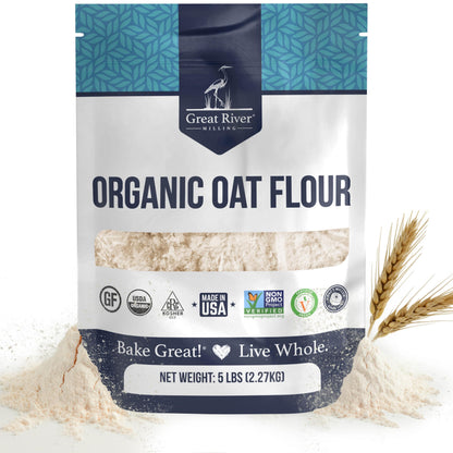 A 5 lb bag of Organic Oat Flour from Great River Milling, made with whole-grain oats and boasting several certifications, displays the “Bake Great! Live Whole.” slogan, shown alongside some organic oat flour and wheat stalks.