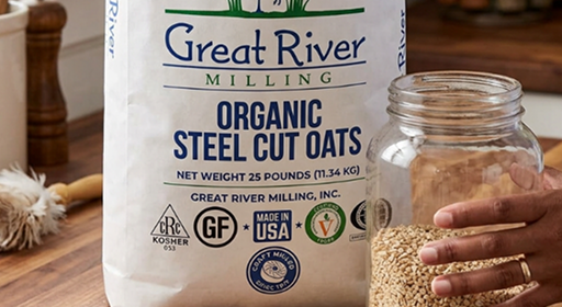 Organic steel cut oats bag labeled Great River Milling with a hand holding a jar of dry oats